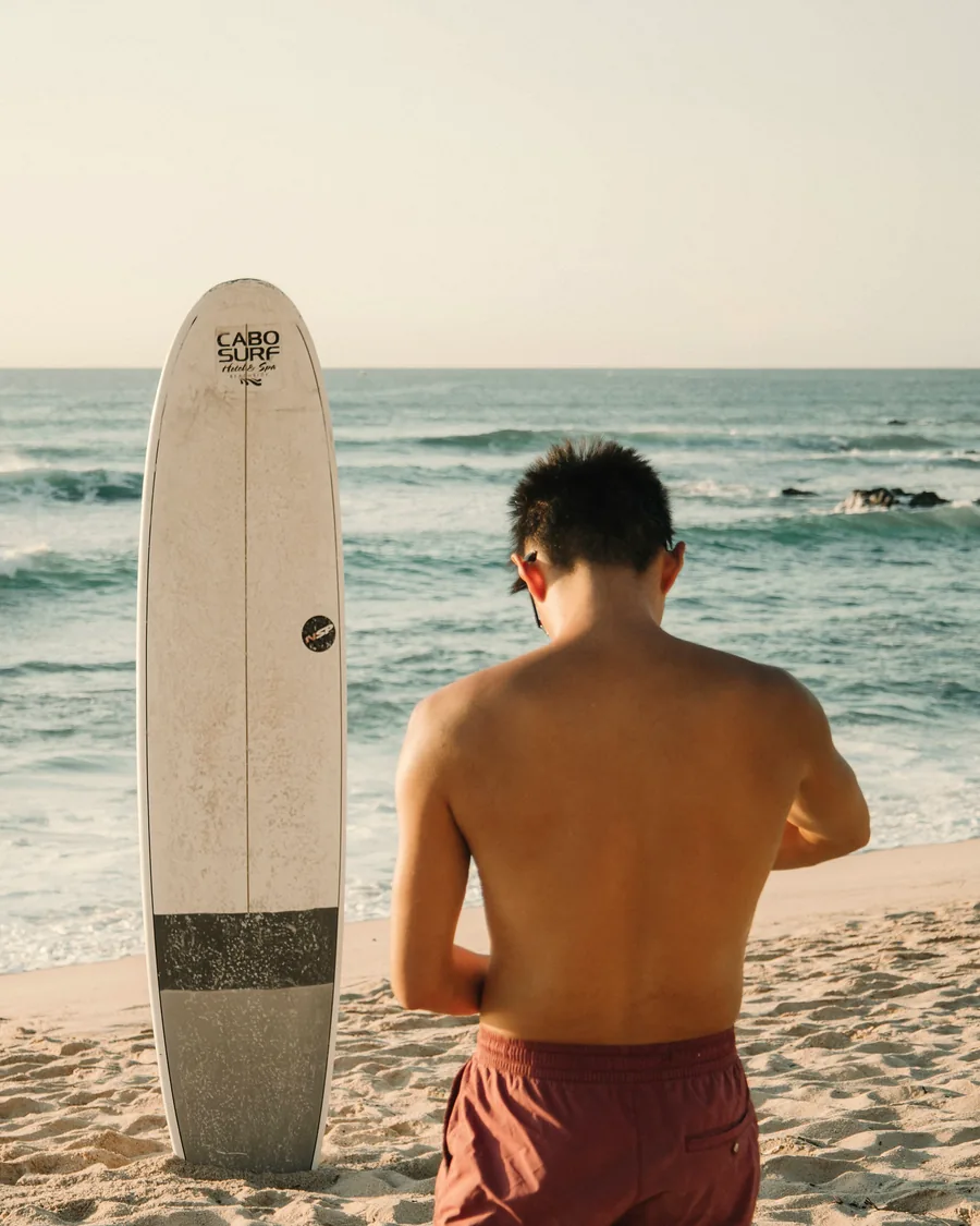 Surfer looking out at the ocean next to a Cabo Surf board