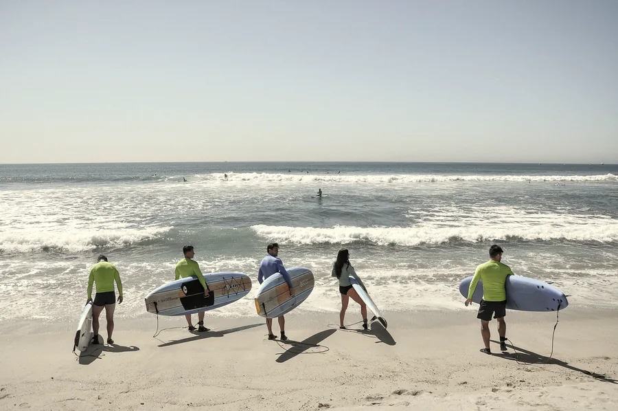 Group of five surfers walking into the water with boards