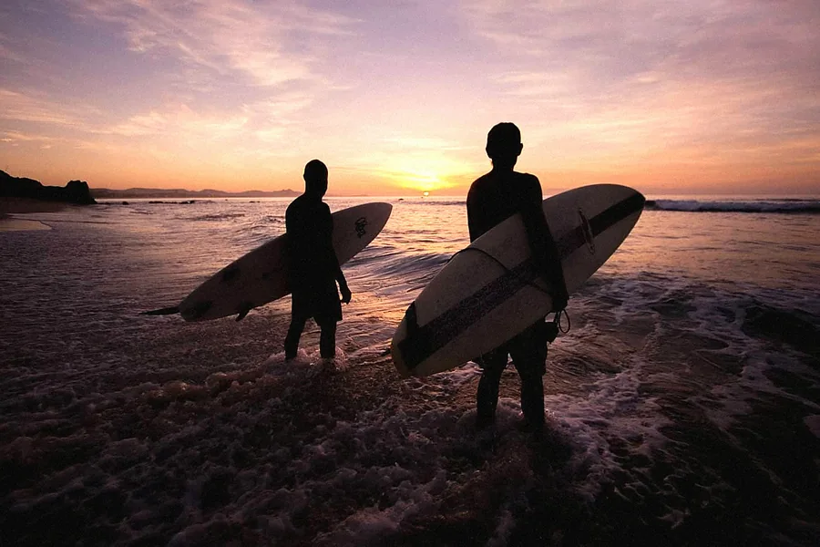 Two surfers silhouetted at sunset carrying their boards into the water